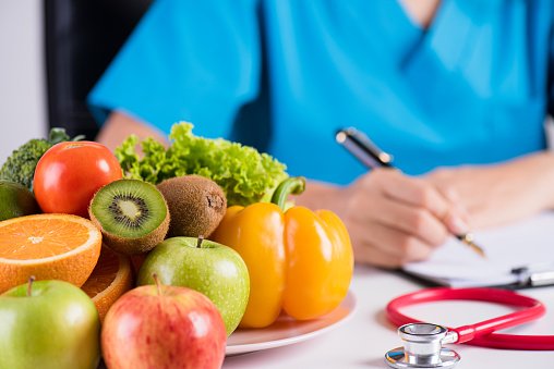 Healthy lifestyle, food and nutrition concept. Close up of fresh vegetables and fruits with stethoscope lying on doctor's desk.
